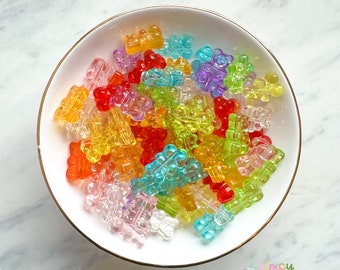 May include: A bowl filled with colorful gummy bear shaped beads. The beads are translucent and come in a variety of colors, including red, orange, yellow, green, blue, and purple.