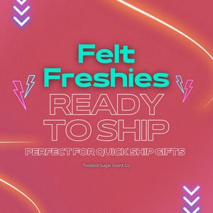 May include: A pink background with the words "Felt Freshies READY TO SHIP" in white and teal. The text is surrounded by lightning bolts and arrows. The text "PERFECT FOR QUICK SHIP GIFTS" is also included.