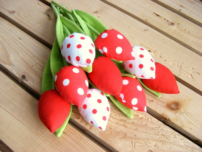 May include: A bouquet of red and white fabric tulips with white polka dots. The tulips are arranged on a wooden surface.