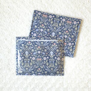 May include: Two rectangular pouches featuring a dark blue background with a dense, repeating floral pattern in shades of pink, light blue, and white. The front pouch includes a clear plastic window and a white zipper closure along the top edge.