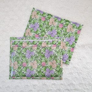 Puede incluir: Dos bolsas con cremallera con un patrón de trébol verde, rosa y morado. Las bolsas están hechas de un material transparente e impermeable.