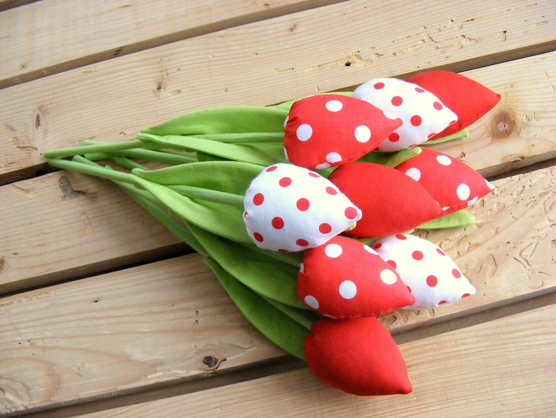 May include: A bouquet of red and white polka dot fabric tulips with green stems. The tulips are arranged on a wooden surface.