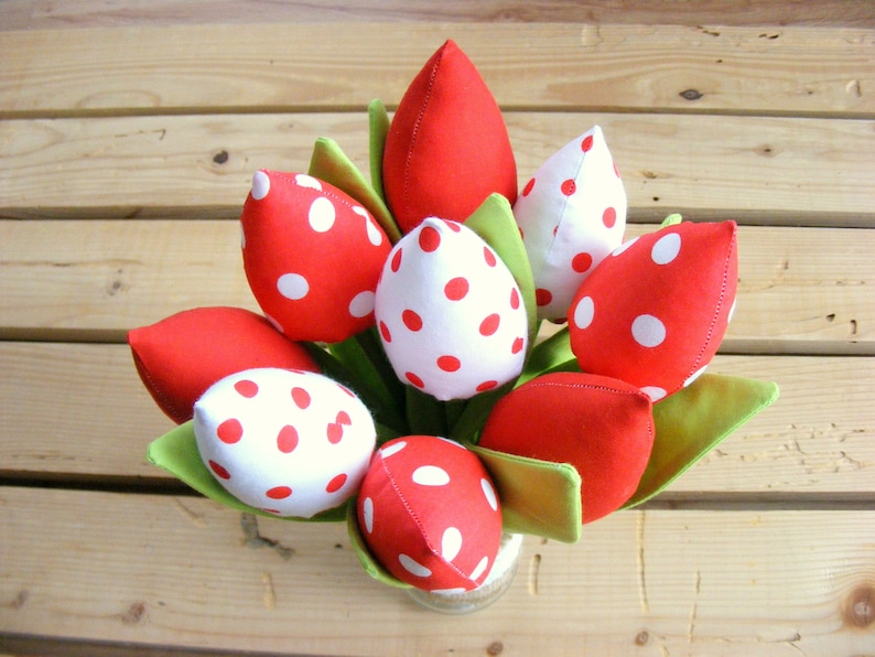 May include: A bouquet of red and white polka dot fabric tulips in a vase. The tulips are arranged in a circle with the stems facing outward.