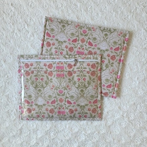 Pode incluir: Duas bolsas com padrão floral. A bolsa maior tem uma frente transparente e um fecho de correr. O padrão floral apresenta flores rosa e vermelhas com folhas verdes sobre um fundo bege. A bolsa menor é visível atrás da maior.