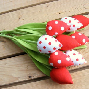 May include: A bouquet of red and white polka dot fabric tulips with green stems. The tulips are arranged on a wooden surface.