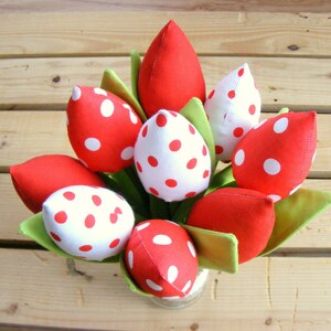 May include: A bouquet of red and white polka dot fabric tulips in a vase. The tulips are arranged in a circular pattern and have green stems.