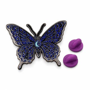 Puede incluir: Un pin de esmalte con forma de mariposa que presenta un fondo de purpurina azul oscuro con contornos negros. Las alas est&aacute;n decoradas con patrones celestiales que incluyen estrellas y lunas crecientes. Una luna creciente azul claro en el centro. Dos cierres morados.