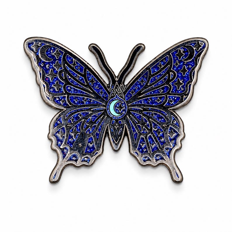 Puede incluir: Un broche de esmalte con forma de mariposa que presenta un fondo de purpurina azul oscuro con contornos de metal negro. Las alas est&aacute;n decoradas con patrones celestiales que incluyen estrellas, lunas crecientes y un icono central.
