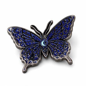 Puede incluir: Un broche de esmalte con forma de mariposa que presenta un fondo azul oscuro brillante con contornos negros. Las alas est&aacute;n decoradas con patrones celestiales que incluyen estrellas y lunas crecientes. Una peque&ntilde;a luna creciente azul claro est&aacute; en el centro.