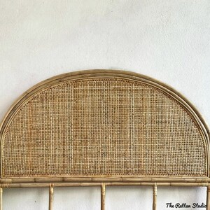 May include: A natural woven rattan headboard with a half-circle shape. The headboard is made of woven rattan with a natural brown color. The headboard is mounted on a white wall. The text "The Rattan Studio" is visible in the bottom right corner of the image.