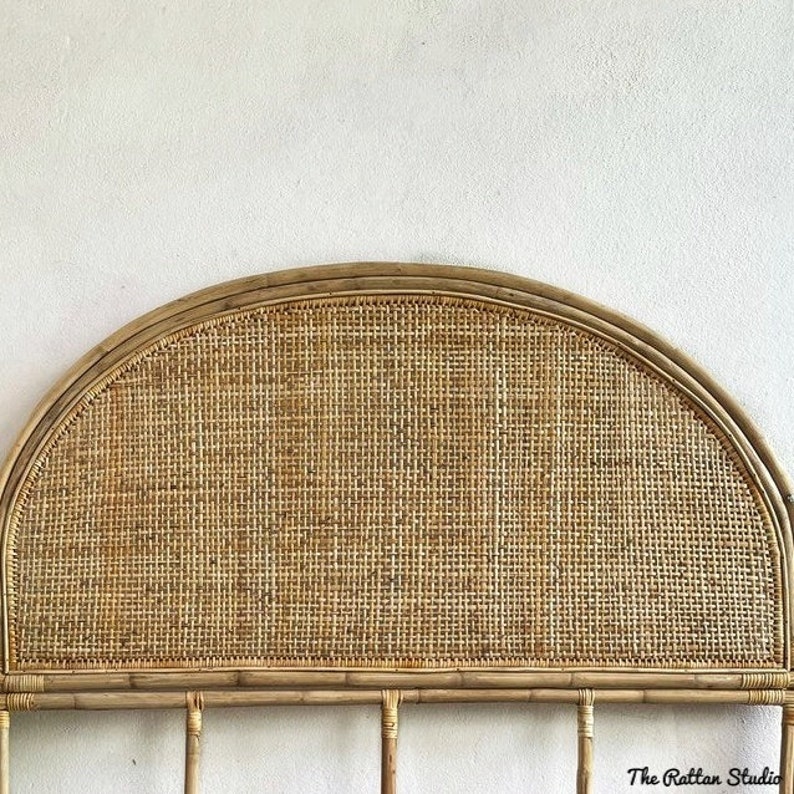 May include: A natural woven rattan headboard with a half-circle shape. The headboard is made of woven rattan with a natural brown color. The headboard is mounted on a white wall. The text "The Rattan Studio" is visible in the bottom right corner of the image.
