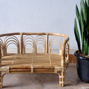 May include: A natural woven rattan pet bed with a rounded shape and a woven design. The bed has a light brown colour and is made of natural materials.