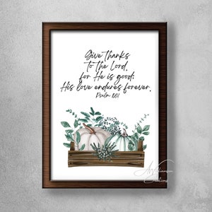 Puede incluir: Una impresión enmarcada con fondo blanco que presenta una ilustración de acuarela de calabazas blancas en una caja de madera con hojas verdes. El texto "Give thanks to the Lord. for He is good: His love endures forever. Psalm 1061" está escrito en letra cursiva negra.