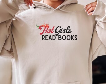 Puede incluir: Sudadera con capucha beige con bolsillo delantero y cordón. El frente presenta el texto "Hot Girls READ BOOKS" en letras rojas y negras, con un diseño de chile.