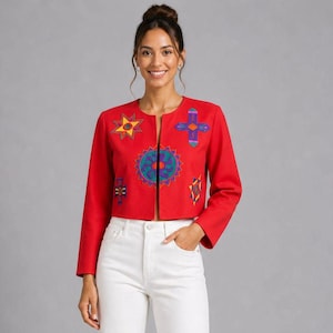May include: A red, open-front jacket with long sleeves and colorful embroidered geometric designs. The jacket features a round design in the center and star and cross-like shapes. The model is wearing white jeans.