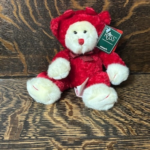 Può includere: Un orsacchiotto di peluche con pelliccia color crema sul viso, sulle mani e sui piedi, e pelliccia rosso brillante sul corpo e sulle orecchie. L'orso presenta un papillon rosso, un naso rosso e un'etichetta verde Russ sull'orecchio con testo bianco.