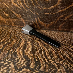May include: A silver and black kitchen utensil with a handle. The utensil is lying on a wooden surface.