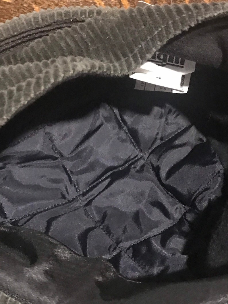 May include: A black corduroy hat with a black quilted lining. The hat has a label that says "REMOVE" and "MADE IN CHINA".