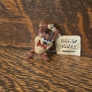 Op de afbeelding: Een bruine Tazmanian Devil sleutelhanger met een metalen ring en een label met de tekst "Looney Tunes" en "applause".