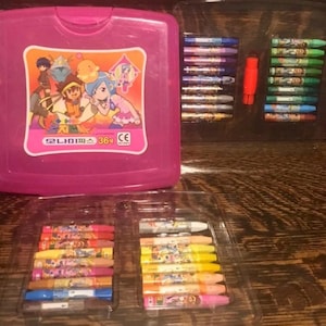 May include: A pink crayon box with a cartoon graphic and the text "모나미파스 36". The box is open, revealing several trays of colorful crayons. The crayons are arranged in rows and columns, with a variety of colors.
