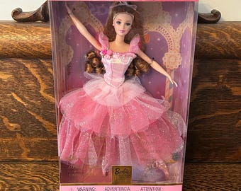 Op de afbeelding: Een Barbie Collector Edition pop in een roze balletoutfit, gepresenteerd in een transparante doos met roze details. De pop heeft bruin haar en een roze tutu met glitter.