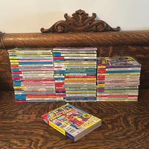 Può includere: Una collezione di fumetti vintage, tra cui Archie's Double Digest e B&V Jumbo Comics, impilati su una superficie di legno. I fumetti presentano copertine colorate con vari titoli e numeri. Lo sfondo include un elemento decorativo in legno.