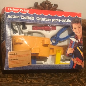 May include: A yellow and blue plastic tool belt with a variety of tools, including a hammer, screwdriver, wrench, and pliers. The box says "Fisher-Price Action Toolbelt Ceinture porte-outils" and "3-7".