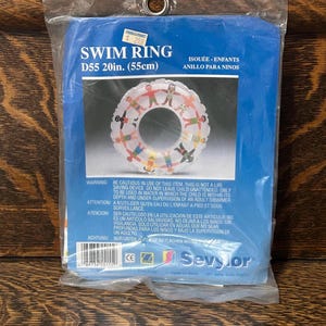 May include: A blue plastic packaging bag containing a white inflatable swim ring with a graphic print of children holding hands. The packaging features the text SWIM RING D55 20in. (55cm) and the Sevylor brand logo with safety warnings.