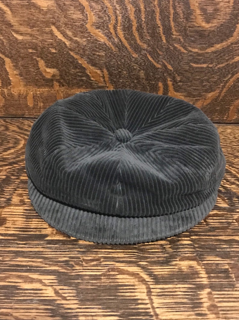 May include: A dark grey corduroy newsboy cap with a rounded crown and a slightly turned-up brim.