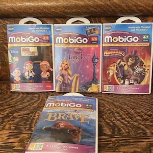 May include: Four VTech MobiGo learning game cartridges featuring Disney characters. The cartridges are white with colorful images of Tangled, Brave, Pirates of the Caribbean, and Madagascar 3. Each cartridge includes 5 learning games and is compatible with MobiGo and MobiGo 2.