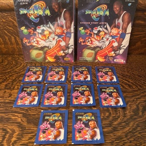 May include: Two Space Jam sticker albums featuring Michael Jordan and the Looney Tunes characters. The albums are in plastic packaging. There are also ten unopened sticker packs with the Space Jam logo and characters.