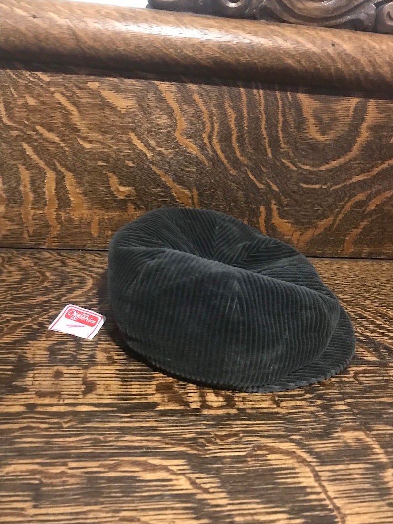 May include: A dark green corduroy newsboy cap with a small red and white tag that says "Off-White" on it.