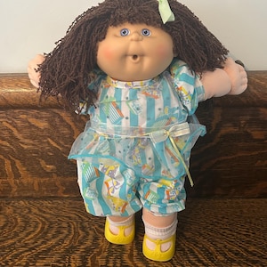 May include: A vintage doll with brown yarn hair, blue eyes, and rosy cheeks. The doll is dressed in a blue and white striped outfit, a matching bow, and yellow shoes. The outfit has a whimsical print.