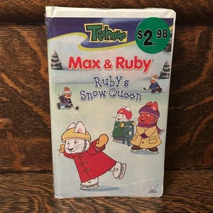 May include: A VHS video tape of the children's animated show "Max & Ruby: Ruby's Snow Queen." The cover features cartoon illustrations of the characters Max and Ruby ice skating, with a green price sticker in the upper right corner.
