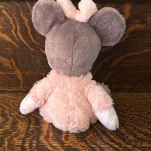 May include: A plush toy mouse with gray ears and head, a pink crown, and a pink body. The mouse has white paws and is made of soft, fuzzy material. The toy is designed for children.
