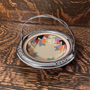 May include: A silver serving dish with a handle and a floral design on the rim. The dish has a white ceramic bowl with a colorful floral pattern inside.