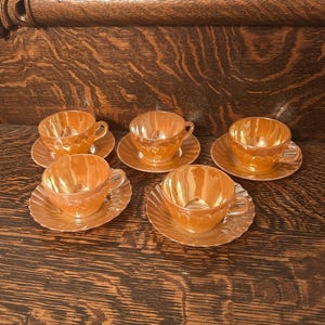 May include: Set of six vintage iridescent peach teacups and saucers. The cups and saucers have a scalloped edge and a delicate floral design.