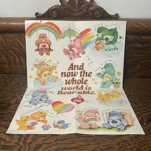 Puede incluir: Un póster blanco que presenta varios personajes de Care Bears en ilustraciones coloridas con arcoíris, nubes y flores. El texto central dice: And now the whole world is Bear-able. Cada personaje está acompañado por un texto de estilo manuscrito.