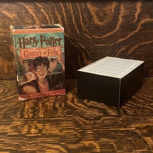 May include: A black cassette tape case with a Harry Potter and the Goblet of Fire book cover on top. The book cover features a colourful illustration of Harry Potter with a wand in his hand.