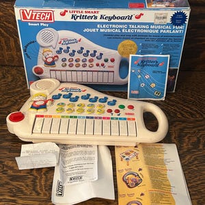 May include: A white VTech Little Smart Kritter's Keyboard toy with a blue and red box. The keyboard has colourful buttons and a handle. The box reads "Electronic Talking Musical Fun!" and "Children play and sing with animals for hours of entertainment!"
