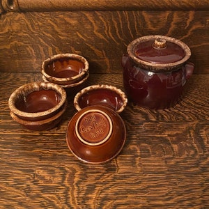 May include: A set of brown and white glazed ceramic bowls and a covered casserole dish. The bowls are stacked and the casserole dish has a lid with a knob. The bowls and casserole dish are labelled "Hull Corn Proof USA".