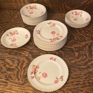 May include: A set of vintage floral china plates with a pink rose pattern. The plates are white with a gold trim and feature a delicate floral design.