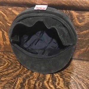 May include: A dark green corduroy newsboy cap with a red label that says "Kangol" on the front.