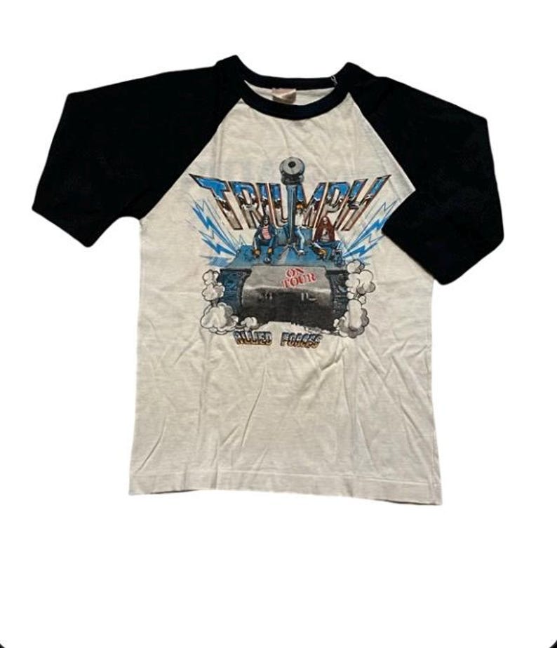 May include: A white and black baseball style t-shirt with a graphic of a tank with the word "TRIUMPH" above it and the words "ON YOUR" and "ALLIED FORCES" below it.