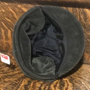 May include: A dark green corduroy newsboy cap with a black lining. The cap is turned inside out, showing the lining.