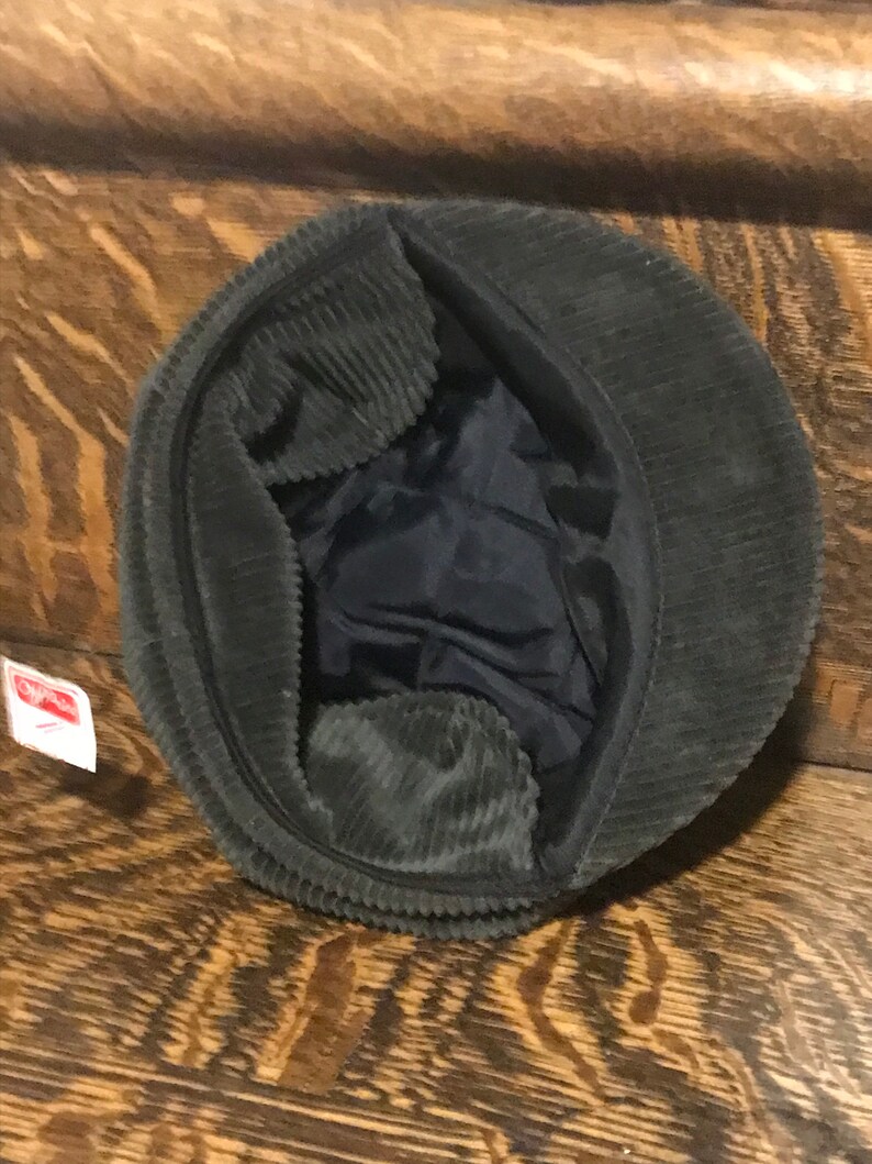 May include: A dark green corduroy newsboy cap with a black lining. The cap is turned inside out, showing the lining.