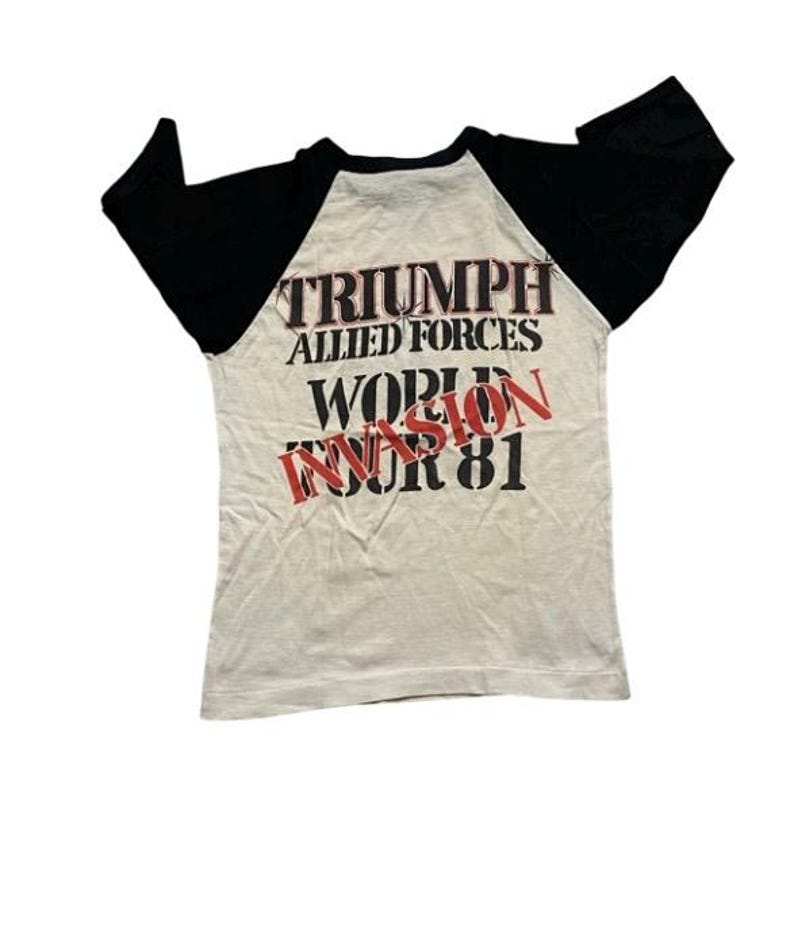 May include: A white t-shirt with black sleeves. The back of the shirt has the text "Triumph Allied Forces World Invasion Tour 81" printed on it.