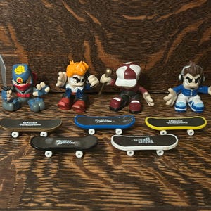 Könnte beinhalten: Eine Sammlung von Miniatur-Skateboarder-Figuren mit passenden Skateboards. Die Figuren sind in verschiedenen Posen und Outfits, darunter ein Ninja und ein Skater mit Kopfhörern. Die Skateboards sind schwarz, blau und gelb.
