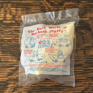 May include: A plastic bag containing a set of Richard Scarry's Busy World finger puppets. The set includes Lowly Worm, Huckle Cat, Hilda Hippo, and Bananas Gorilla. The bag features a Kid's Picknic! logo and the text "Get one in every".