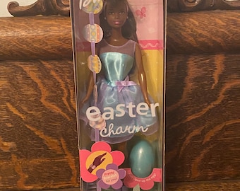 Könnte beinhalten: Eine Barbie-Puppe in einem hellblauen und violetten Kleid mit einem blauen Osterei. Die Schachtel trägt den Text "Barbie Easter Charm" und "Special Edition".